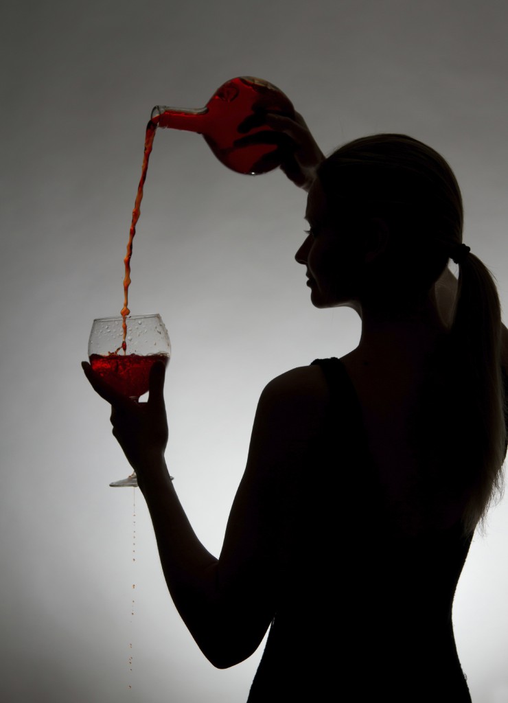 Woman pouring red wine from bottle into a glass on a gray background.