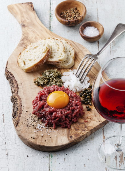 Beef tartare with capers and fresh onion on olive wood board with wine